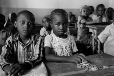 Portrait d'une petite fille et d'un petit garçon africains assis à leur table-banc en classe